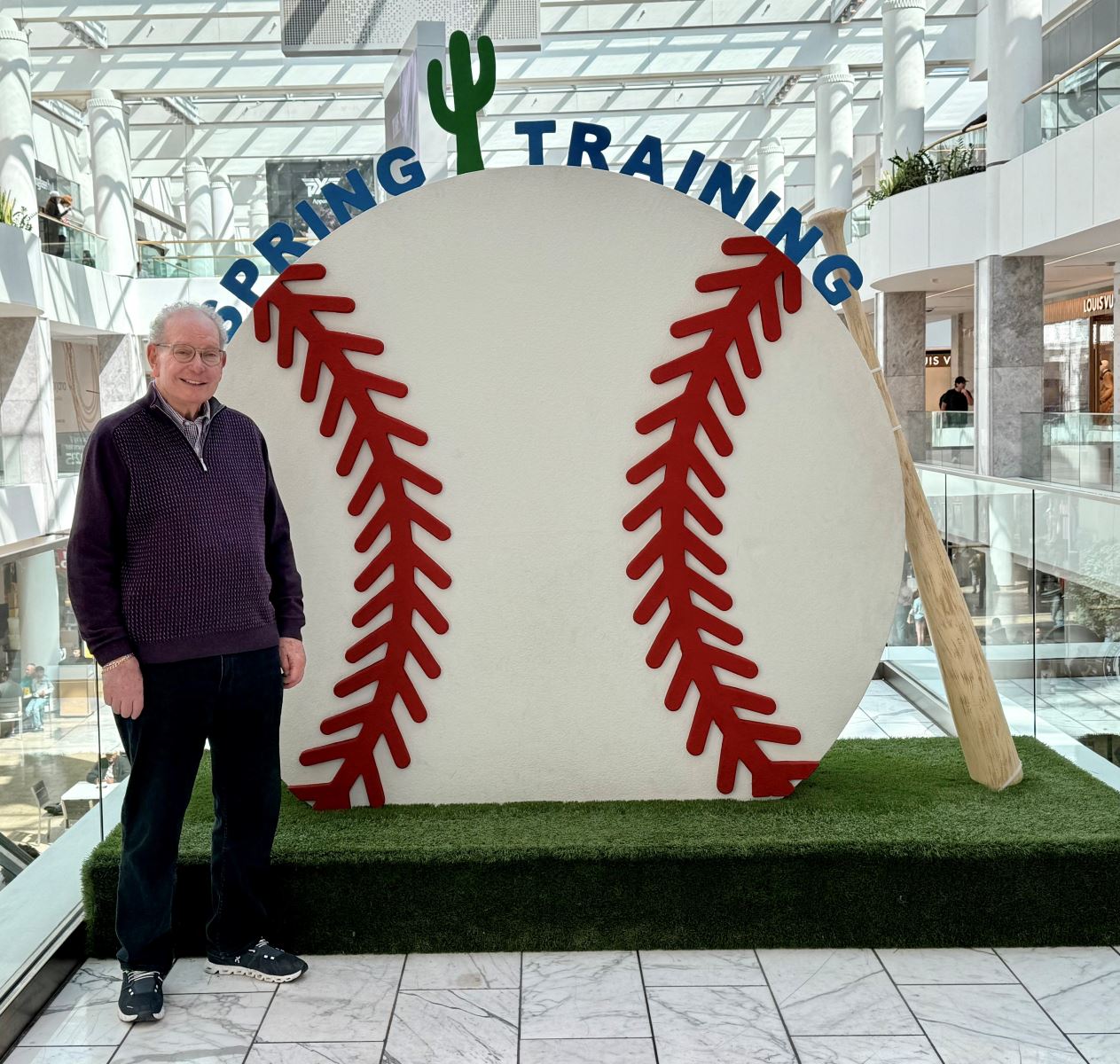 A person standing in front of a large baseball signAI-generated content may be incorrect.